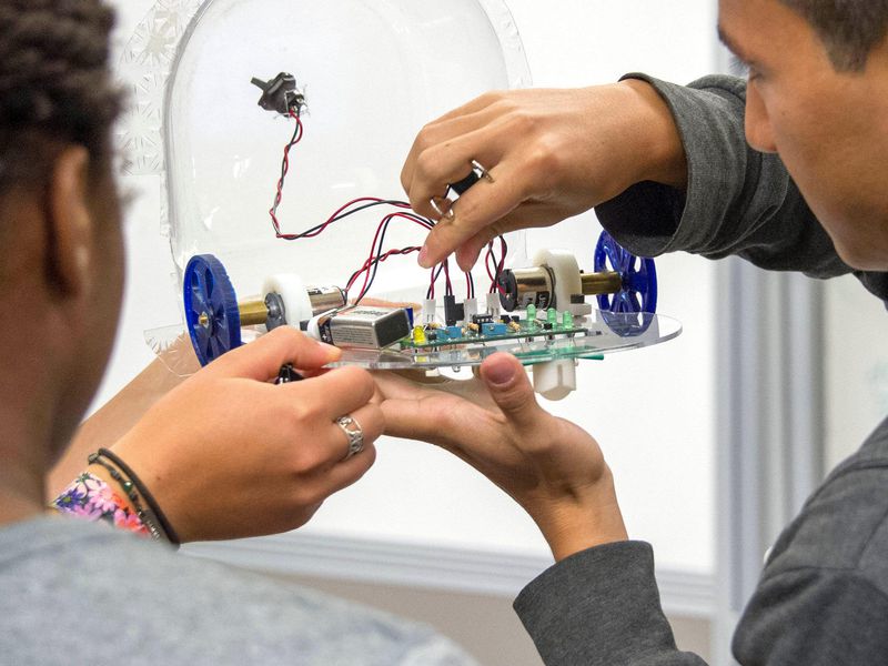 Three students huddle together to work on connecting wires to a circuit board in an ENGS 21 class.
