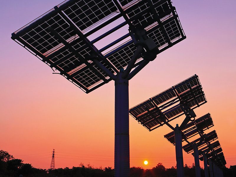 Silhouette of solar panel trees against a vibrant orange and purple sunset sky.